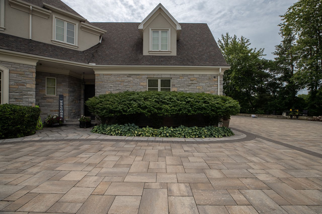 Residential property with large paver driveway and front entrance with green hedges