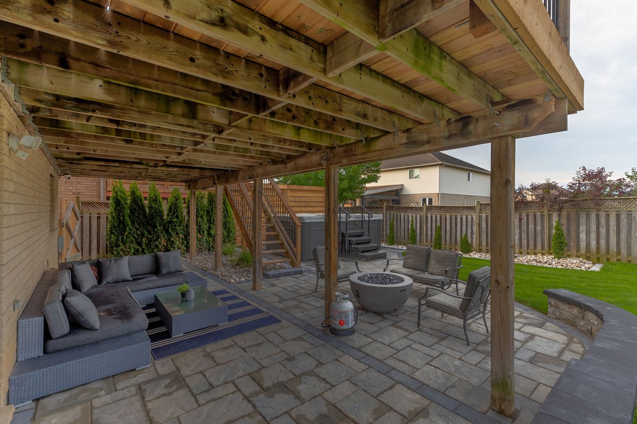 Residential backyard view of paver patio, fire pit, privacy fence, wooden deck and healthy green grass.